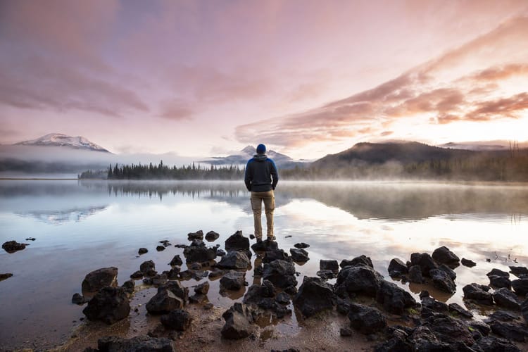 slow travel by a man standing on the bank of a calm lake exhibiting mindful RV living